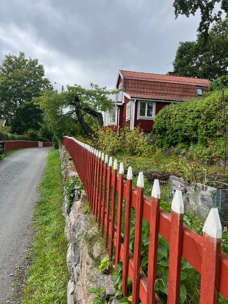 Traditional red wooden house with white trim and red picket fence along a gravel road in Furusund, Stockholm Archipelago Trail